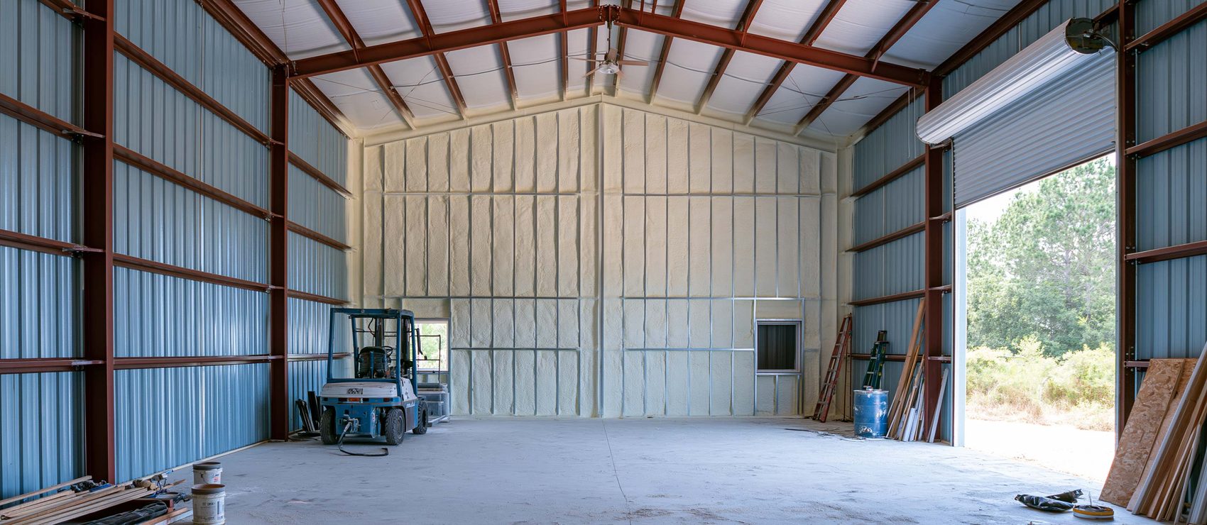 Cream closed-cell spray foam covering the end wall of a steel building while the side walls remain bare metal