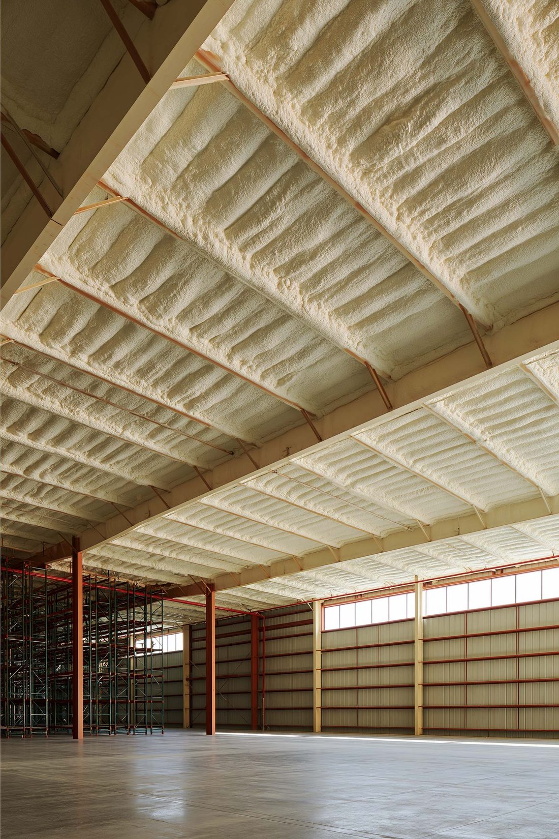 A steel warehouse with spray foam across the roof deck above pallet racking