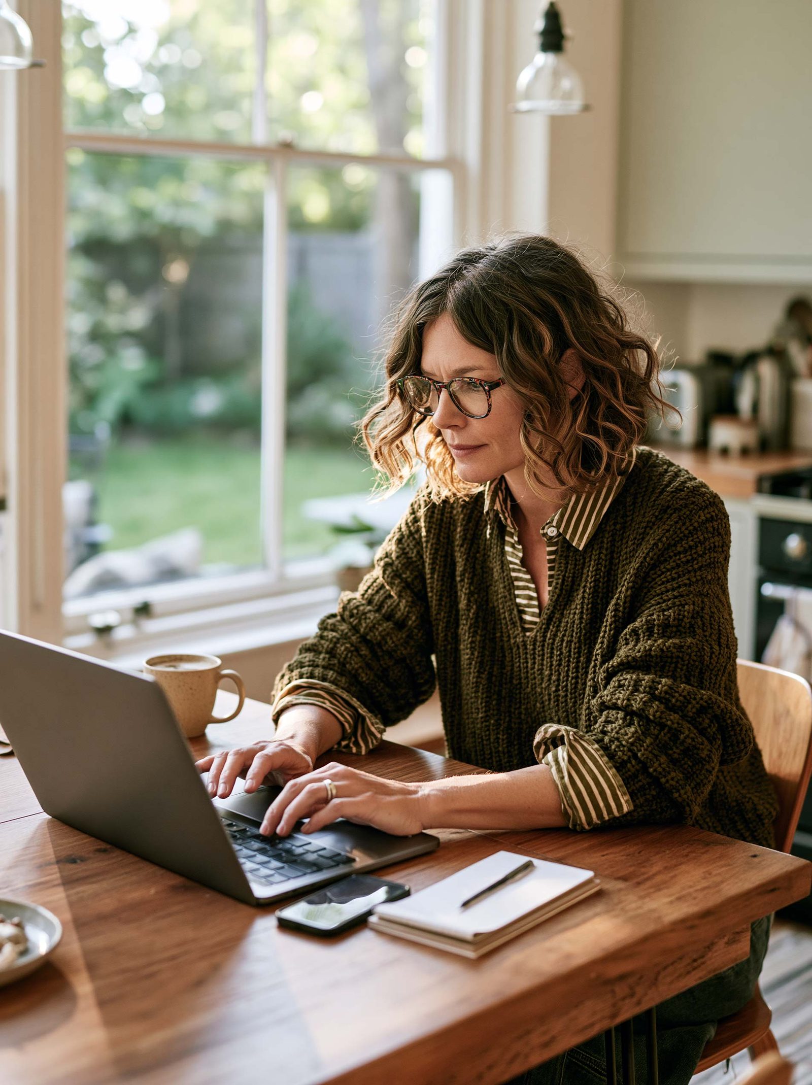 A homeowner at a sunlit kitchen table with a laptop and a mug of coffee